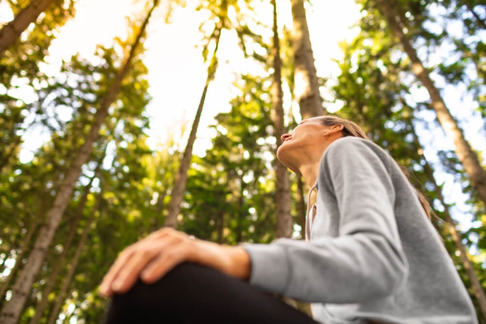 Woman sitting on the ground in the forest as part of nature therapy sessions